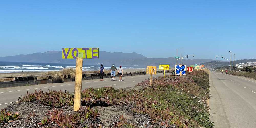 Image of the Great Highway, with a median in the middle of the photo. In the median, there are various political signs that urge people to vote.