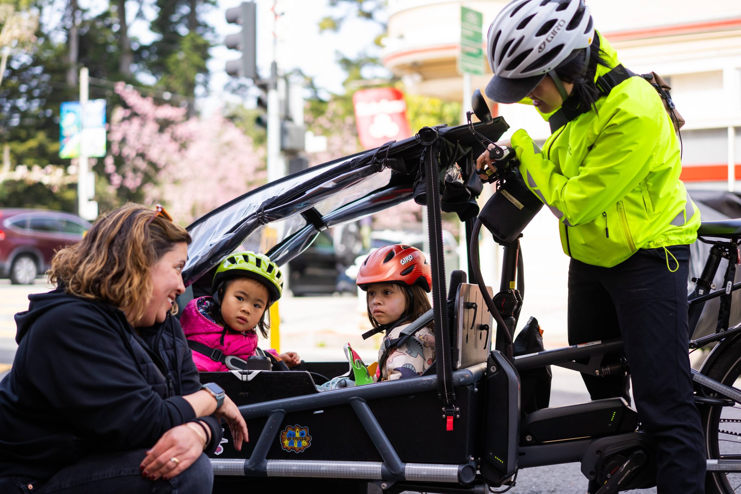 Two adults smiling at 2 children inside a cargo bike.
