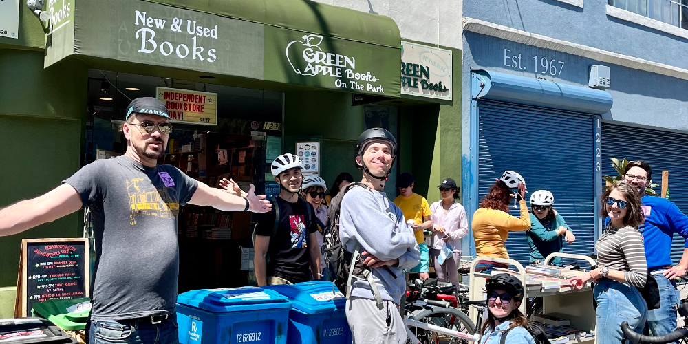 A crowd of people wearing bike helmets stand in front of Green Apple Bookstore