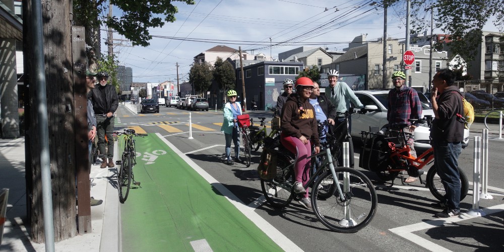 a group of people with bikes stand to the side of a bike lane