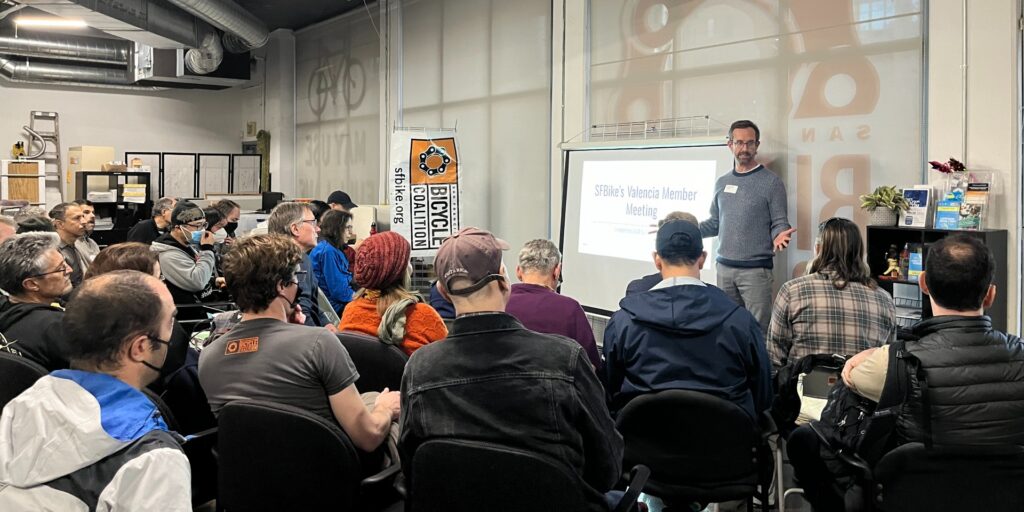 Photo of people sitting in SFBike office, facing a projector screen and speaker.