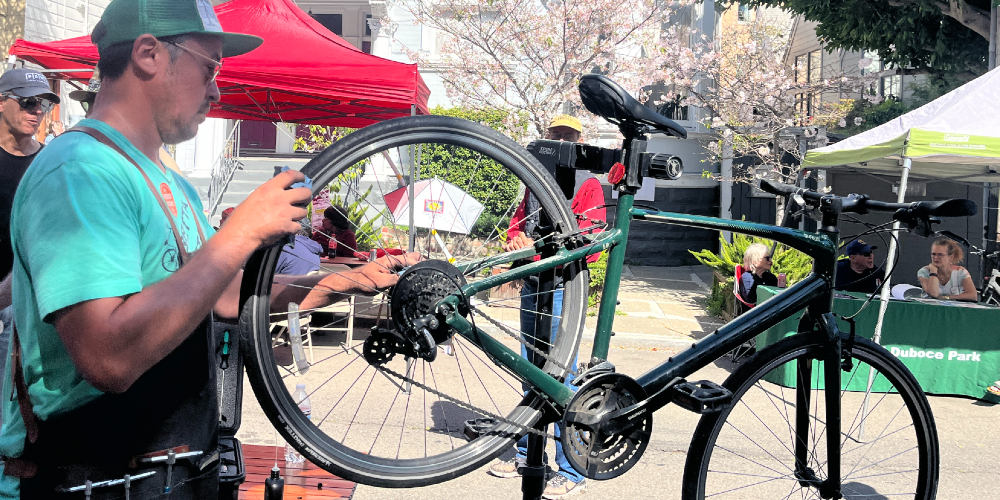 A person in a hat and apron inspects a bike in a repair stand.