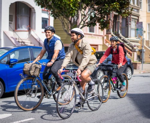 three people bike on a street in front of San Francisco houses