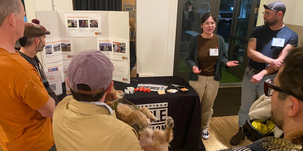 a group of six people standing in a circle and talking in front of a display board