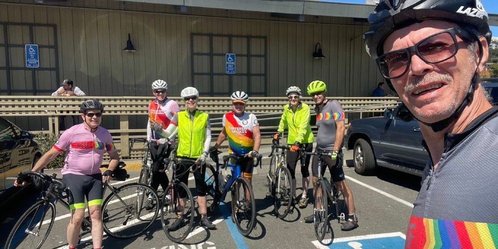 A group of people stand together with their bikes. Many are wearing bright yellow and rainbow colors.