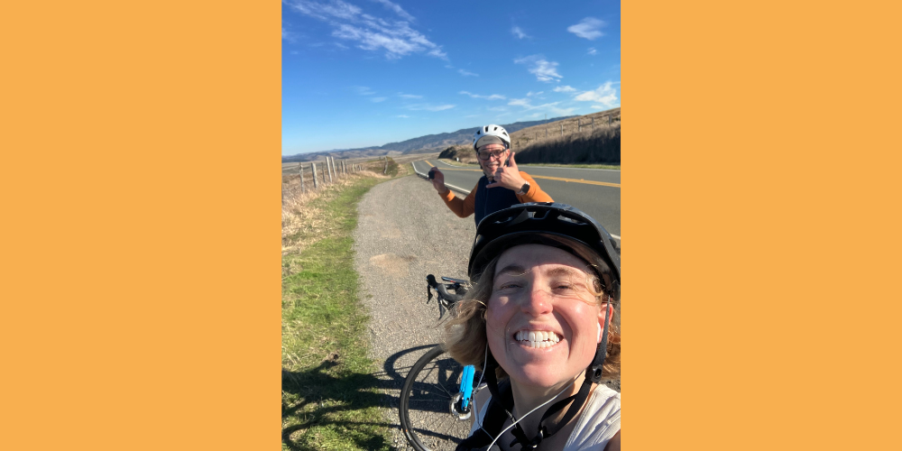 Two people stand on the side of a road with their bikes smiling